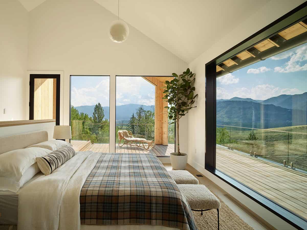 Bedroom with plaid throw and glass wall overlooking mountains and deck