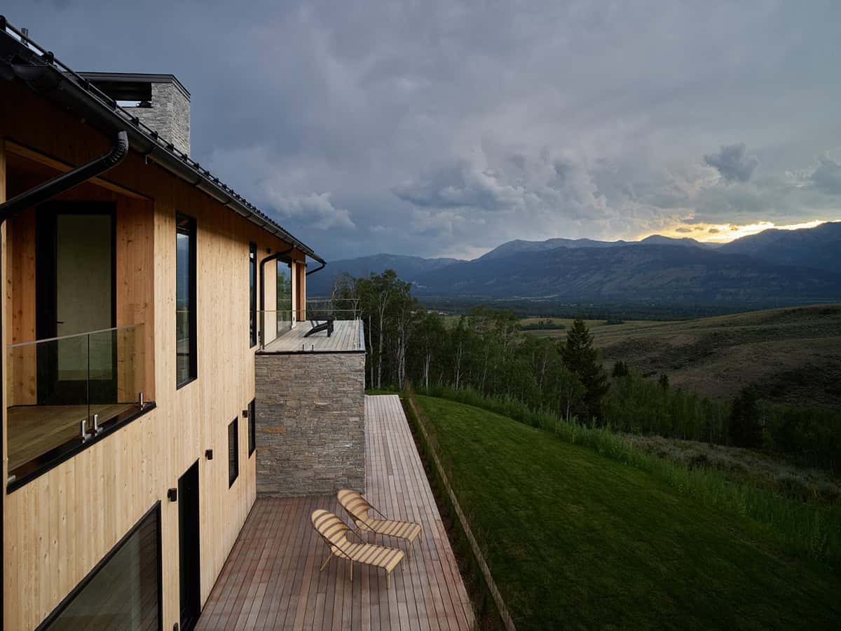 Wood-clad home exterior with deck chairs overlooking valley at dusk