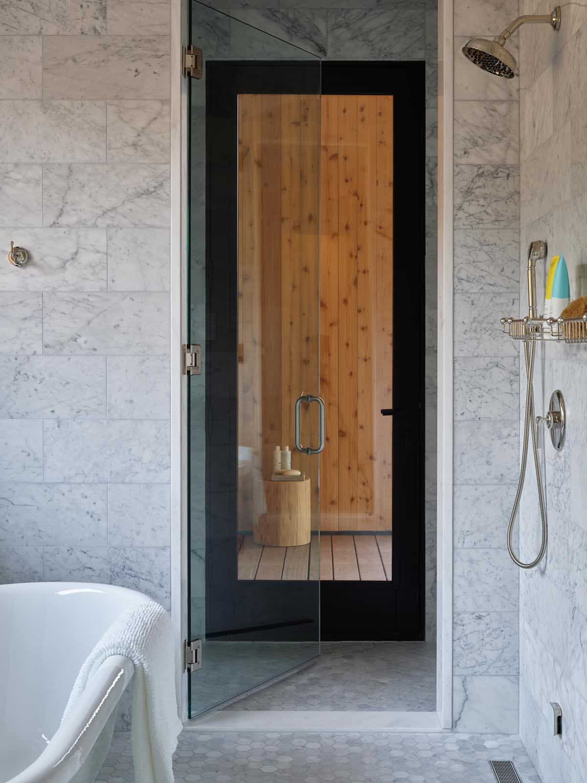 Marble bathroom with glass shower door and wood-paneled sauna view