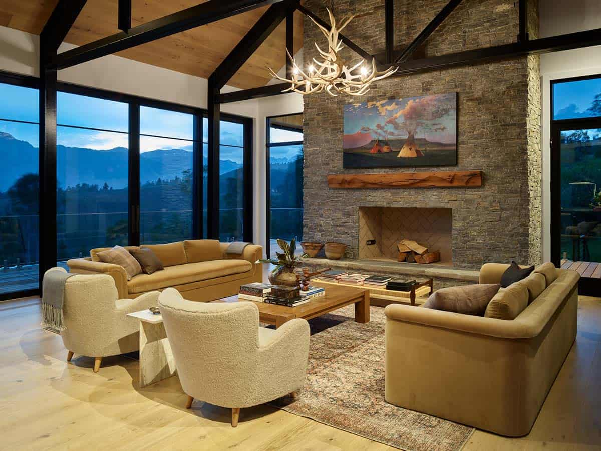 Living room with stone fireplace, antler chandelier, and evening mountain views