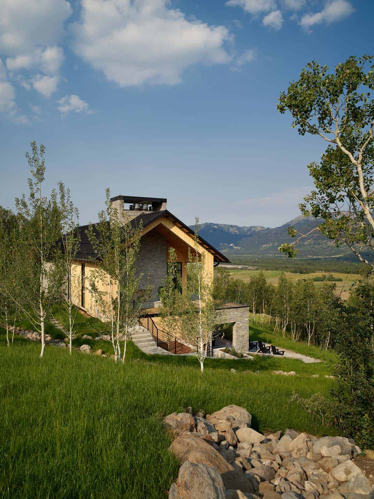 Stone and wood home nestled in green hillside with mountain backdrop