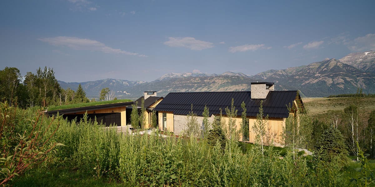 Wood and stone home with black roof set against Teton mountain range