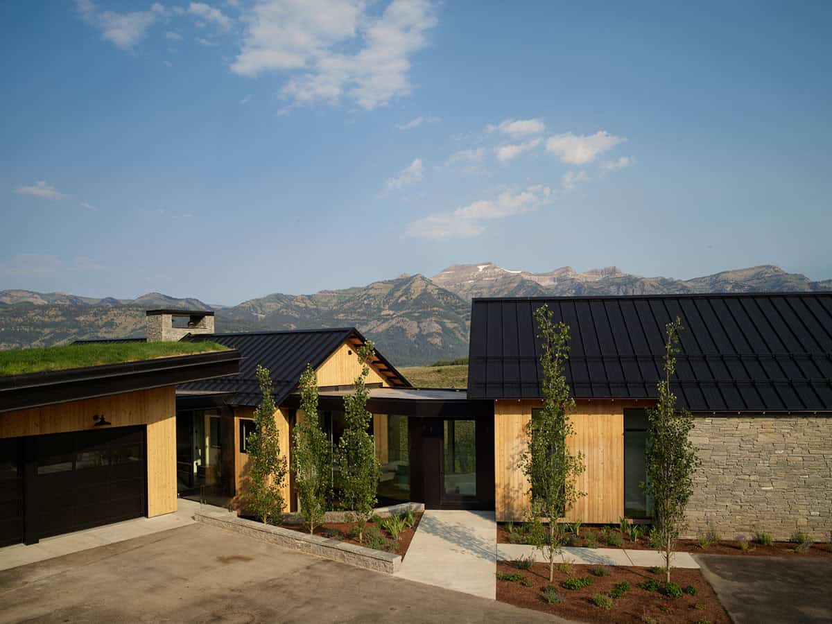 Wood-clad home entrance with black garage door and landscaped walkway