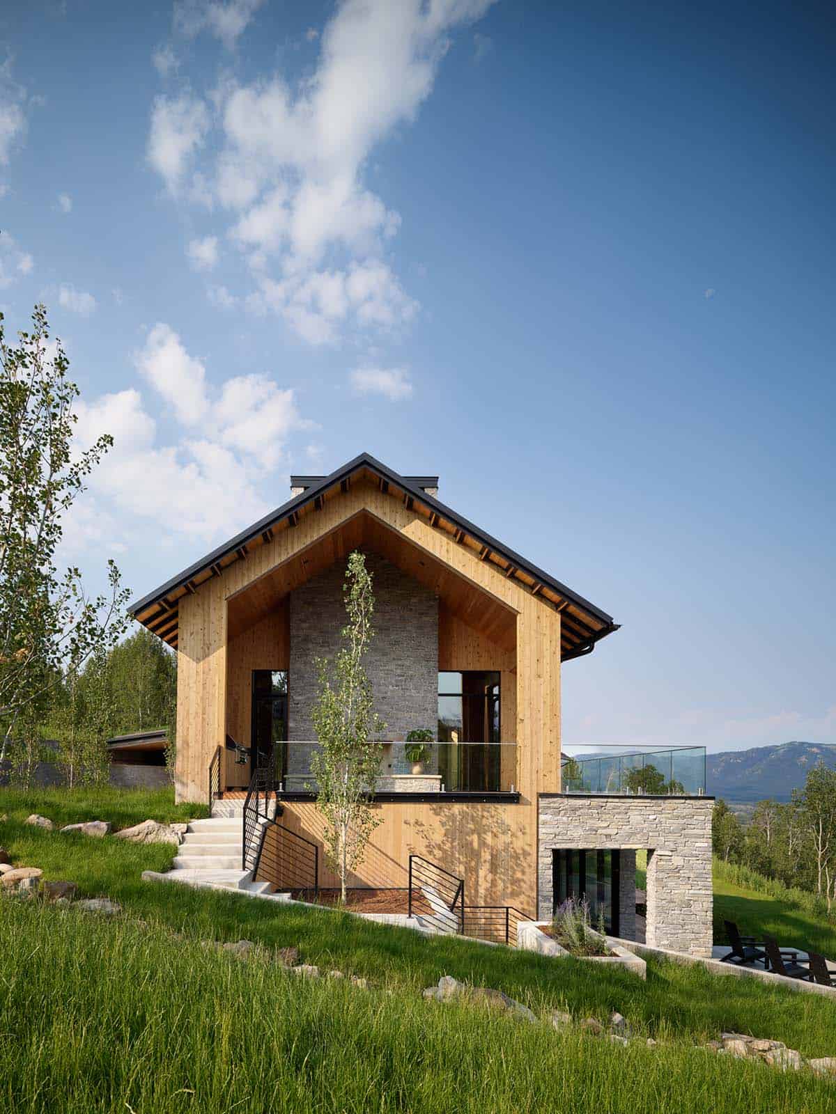 Two-story wood and stone home exterior with green roof and mountain view