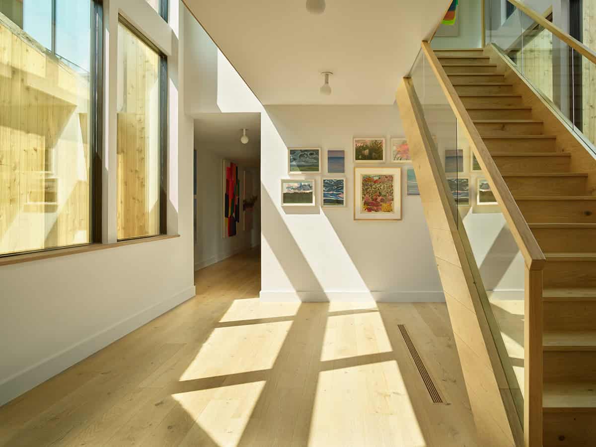 Sunlit hallway with gallery wall and wood staircase behind glass railing