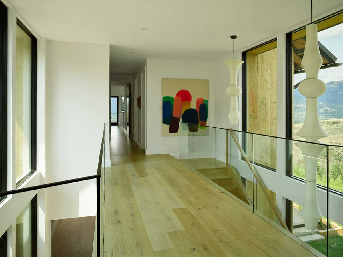 Upper hallway with glass railing, colorful artwork, and pendant lighting