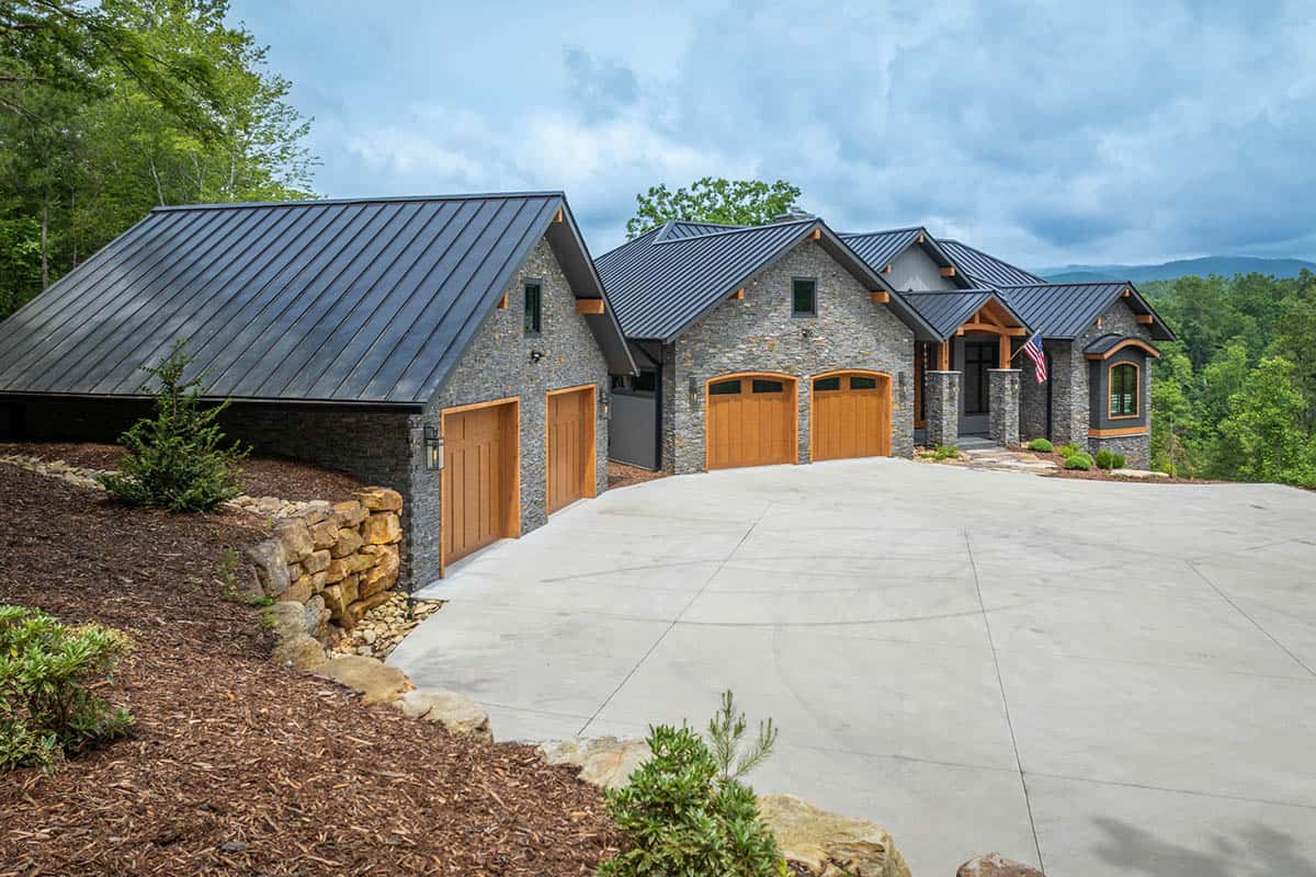 Stone and timber mountain home with dark metal roof and three-car garage at end of long driveway