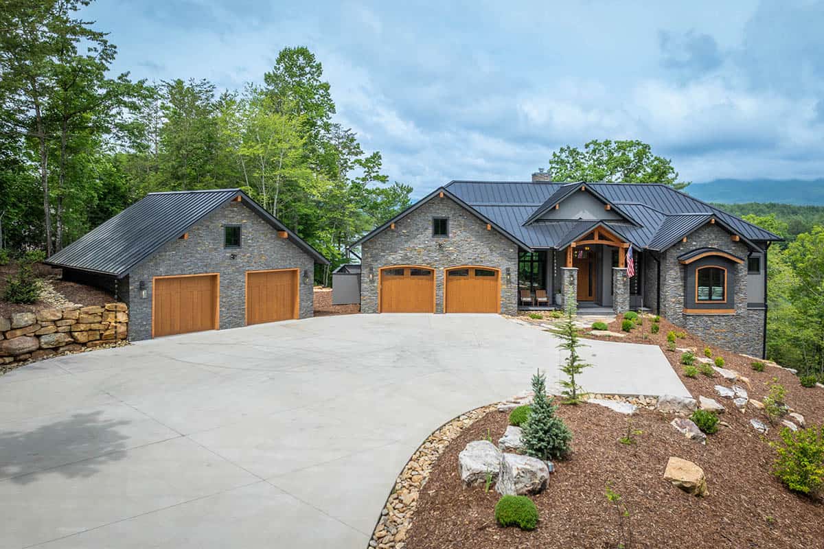 Front view of stone mountain house with steep gabled metal roofs and wood garage doors