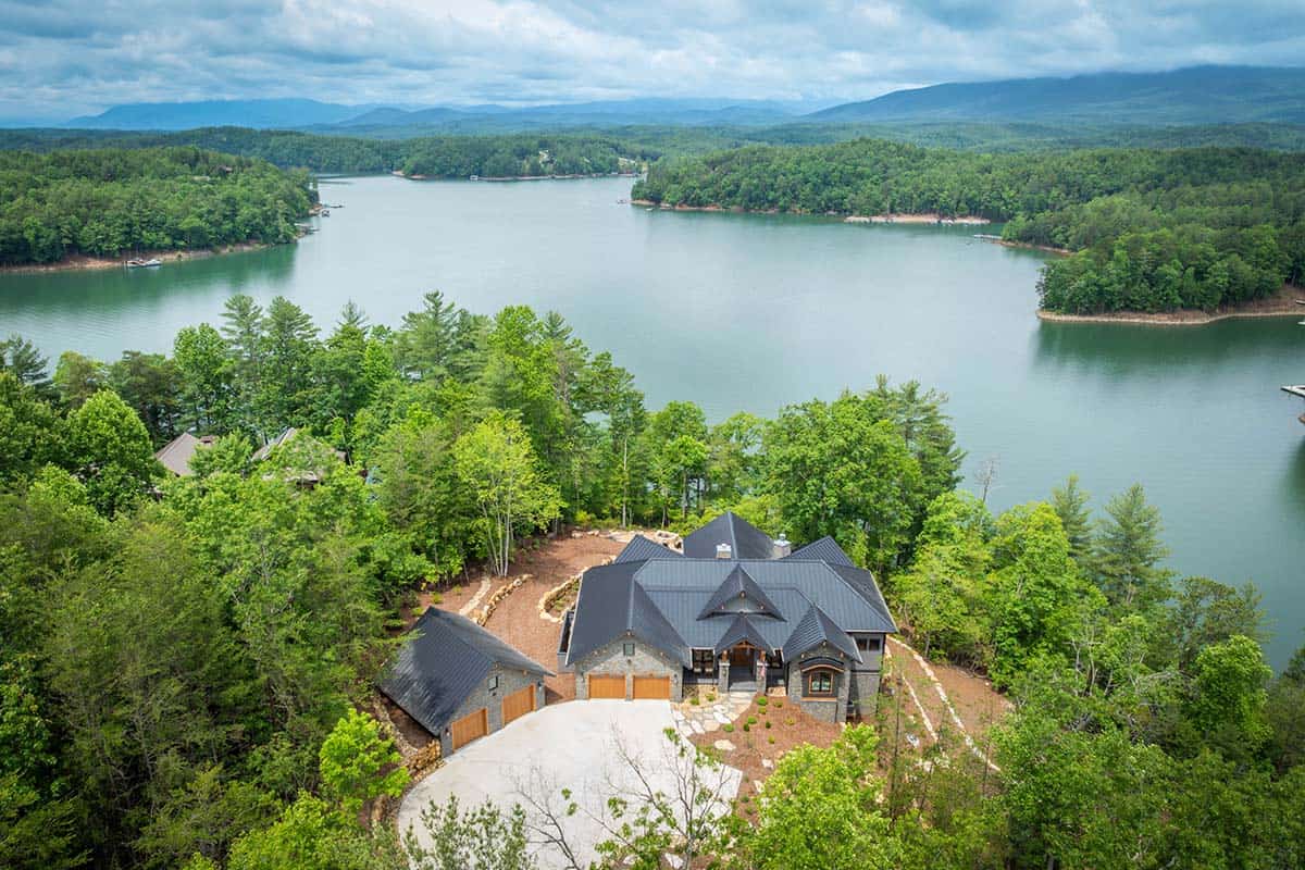 Aerial view of mountain lake house surrounded by forest with lake and mountains in background