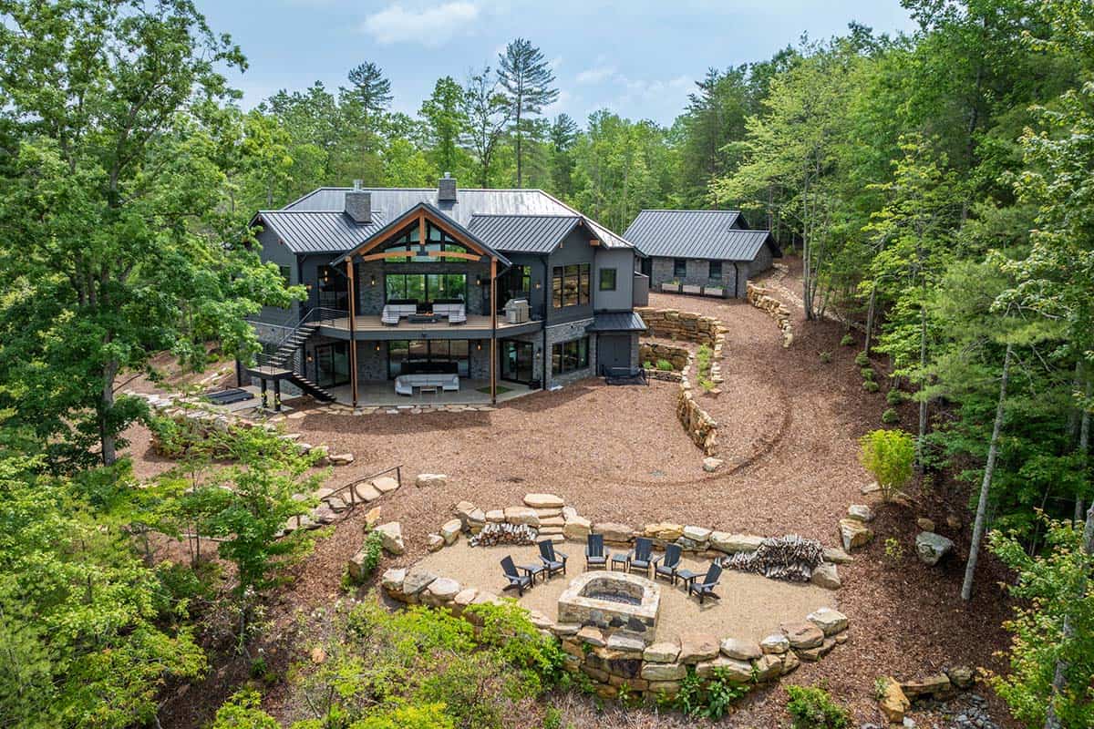 Rear aerial view of contemporary mountain home with covered deck and stone fire pit patio