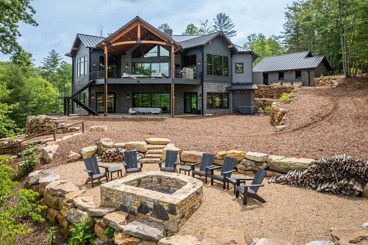 Rear view of home's covered deck with timber-frame gable and stone fire pit surrounded by chairs