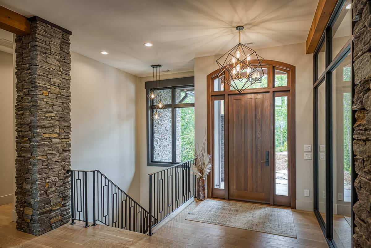 Entry foyer with wood front door, geometric pendant light, and stone accent column
