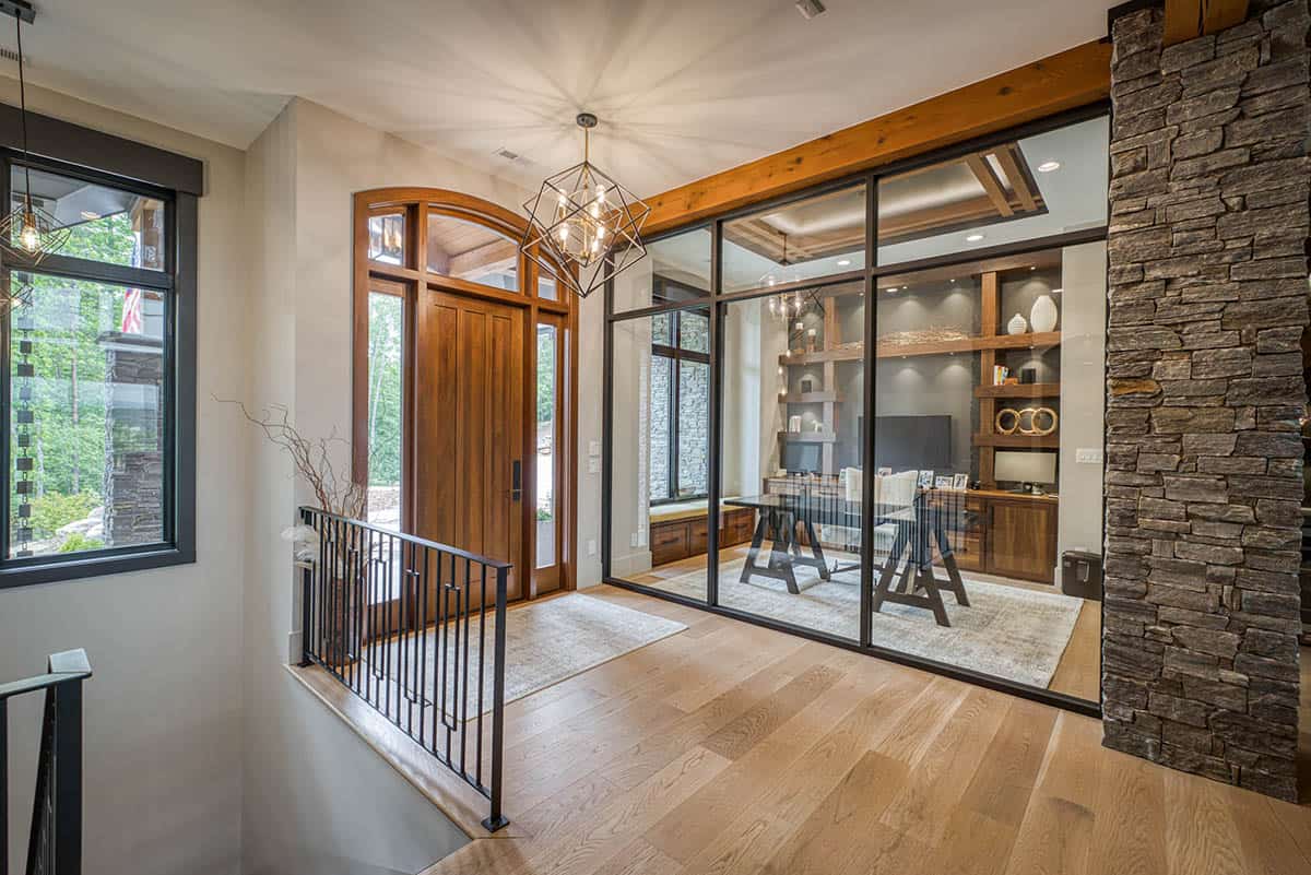 Foyer view into glass-walled home office with wood beam and stone column
