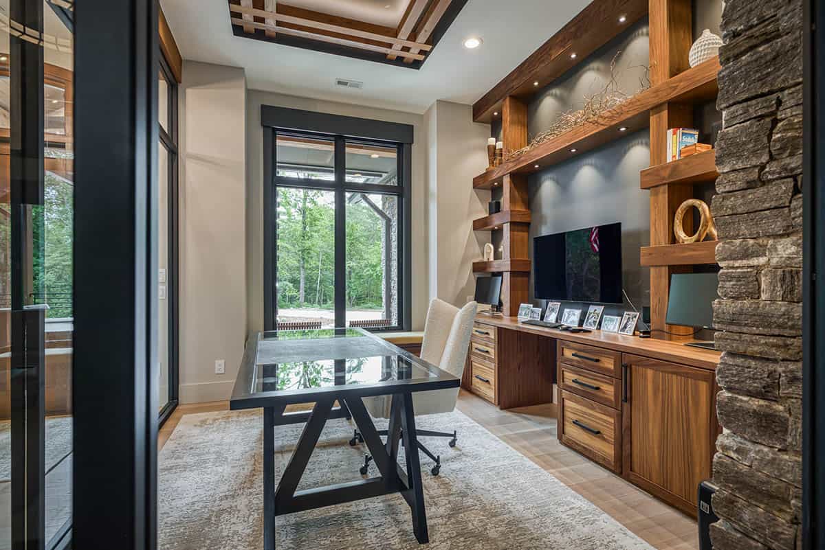 Home office with built-in walnut shelving, glass-top desk, and window view of trees
