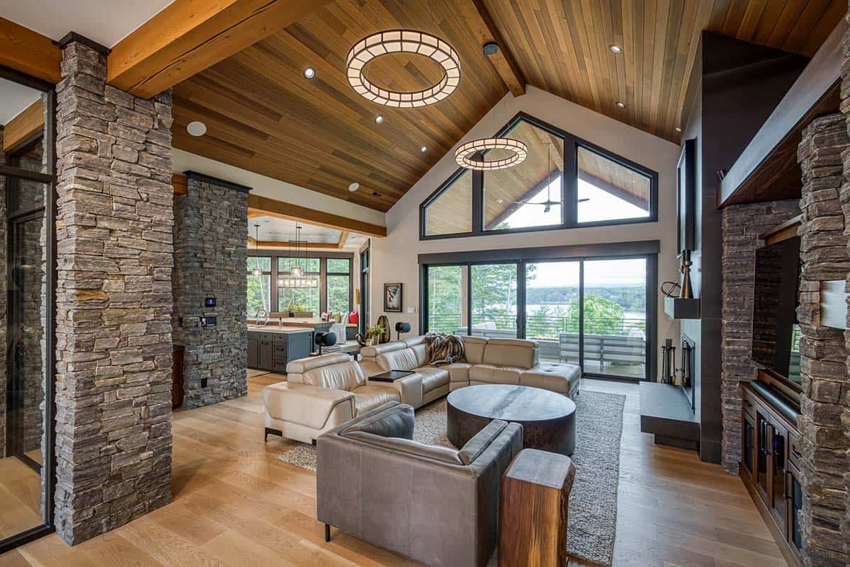 Vaulted great room with stone columns, wood ceiling, leather sectional, and lake view