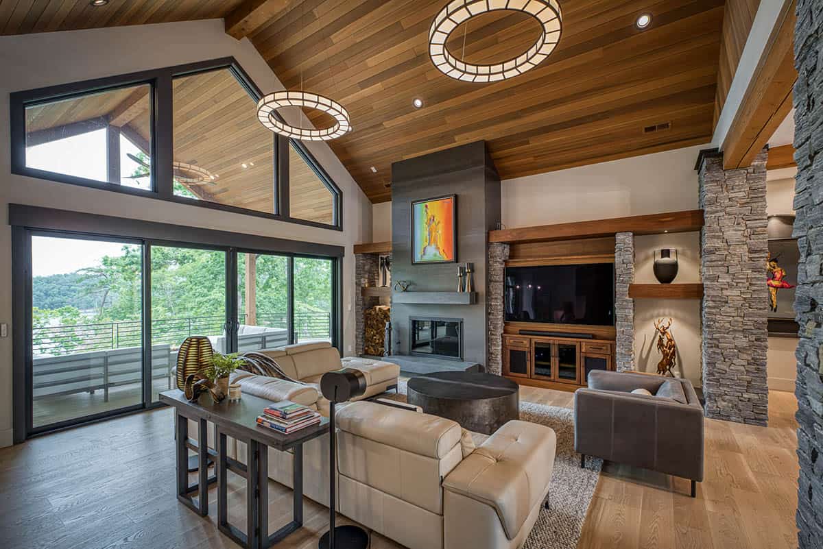 Living room with stone fireplace, mounted TV, wood ceiling, and floor-to-ceiling windows