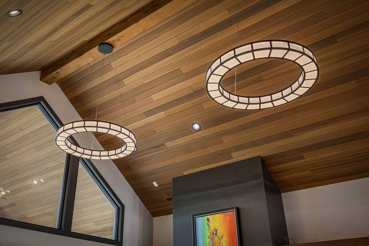 Wood-clad vaulted ceiling with two ring-shaped pendant lights and colorful artwork below