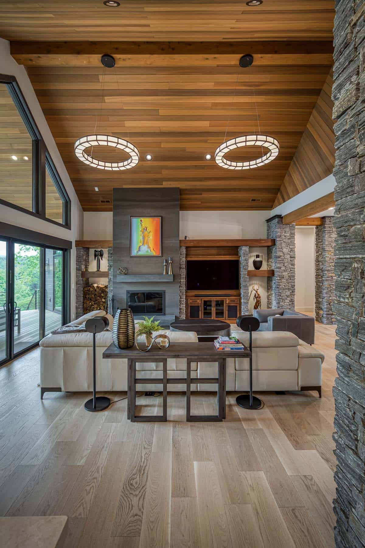 Wide view of living room with vaulted wood ceiling, stone columns, fireplace, and sectional