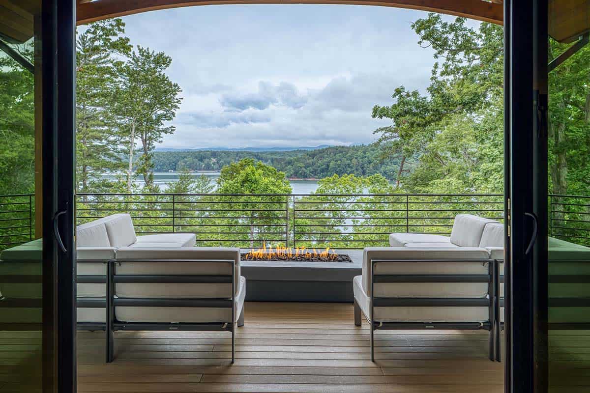 Covered deck with outdoor seating and fire table framed by timber archway overlooking the lake