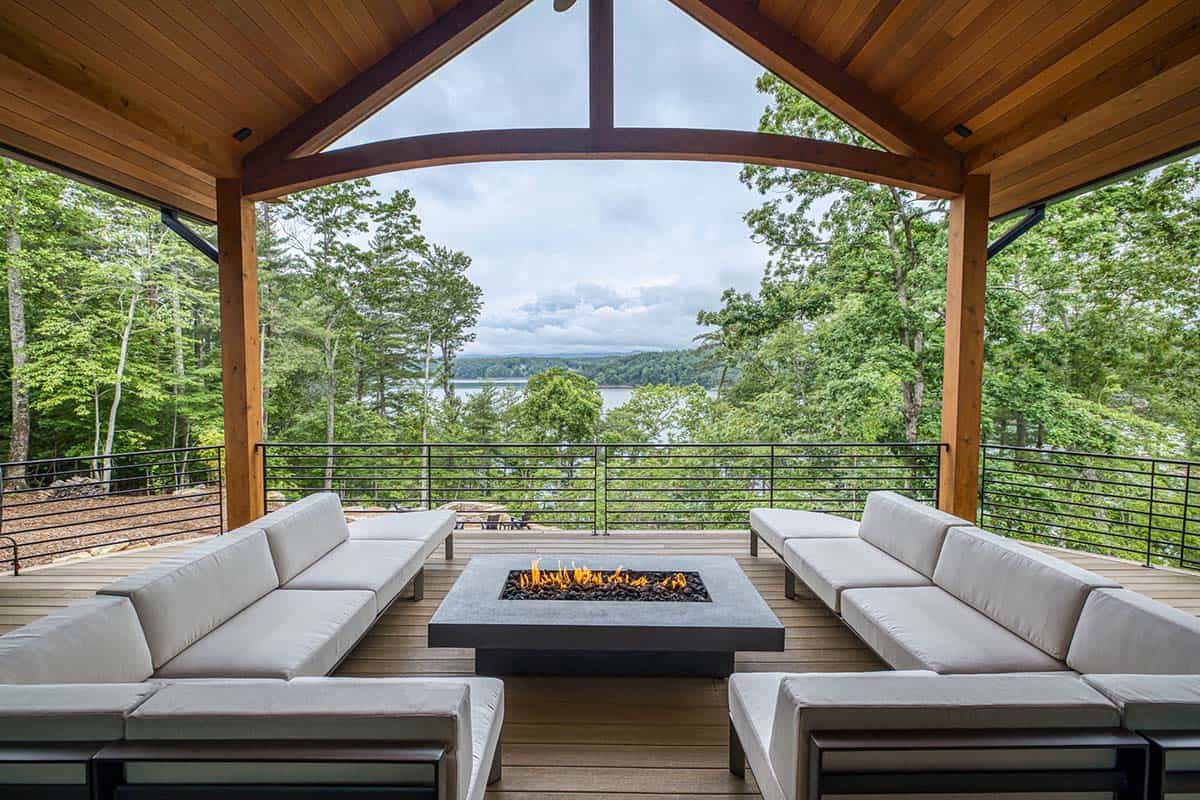 Covered outdoor lounge with sectional sofas around a fire table and forest and lake view