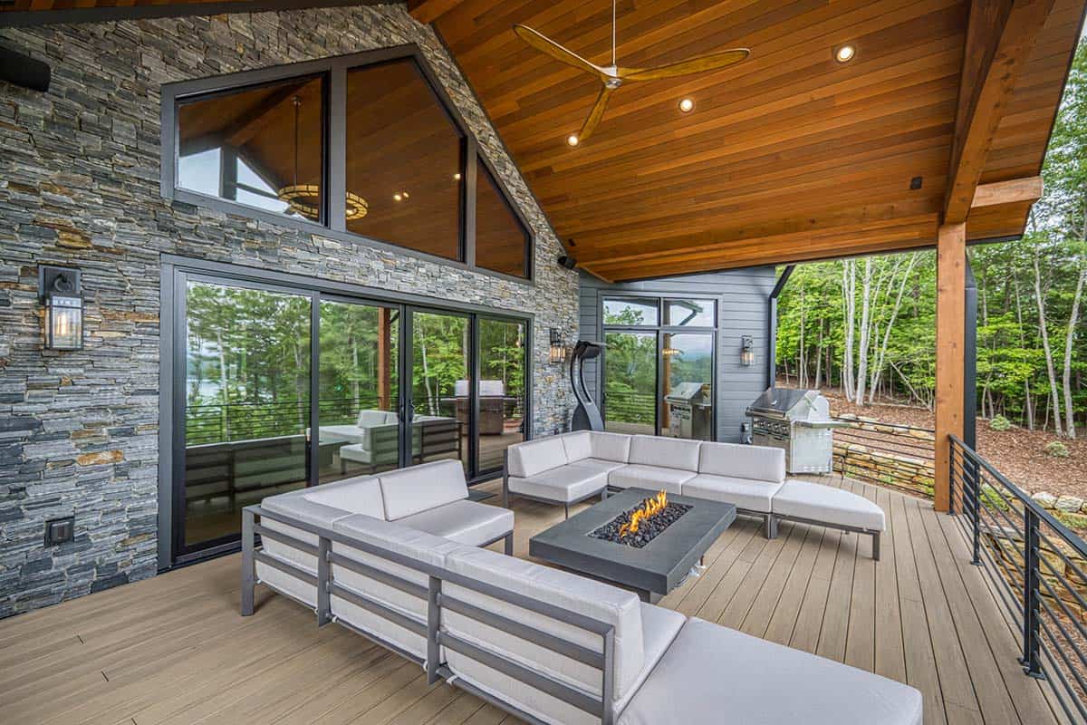 Covered outdoor living space with sectional sofas, fire table, ceiling fan, and grills nearby