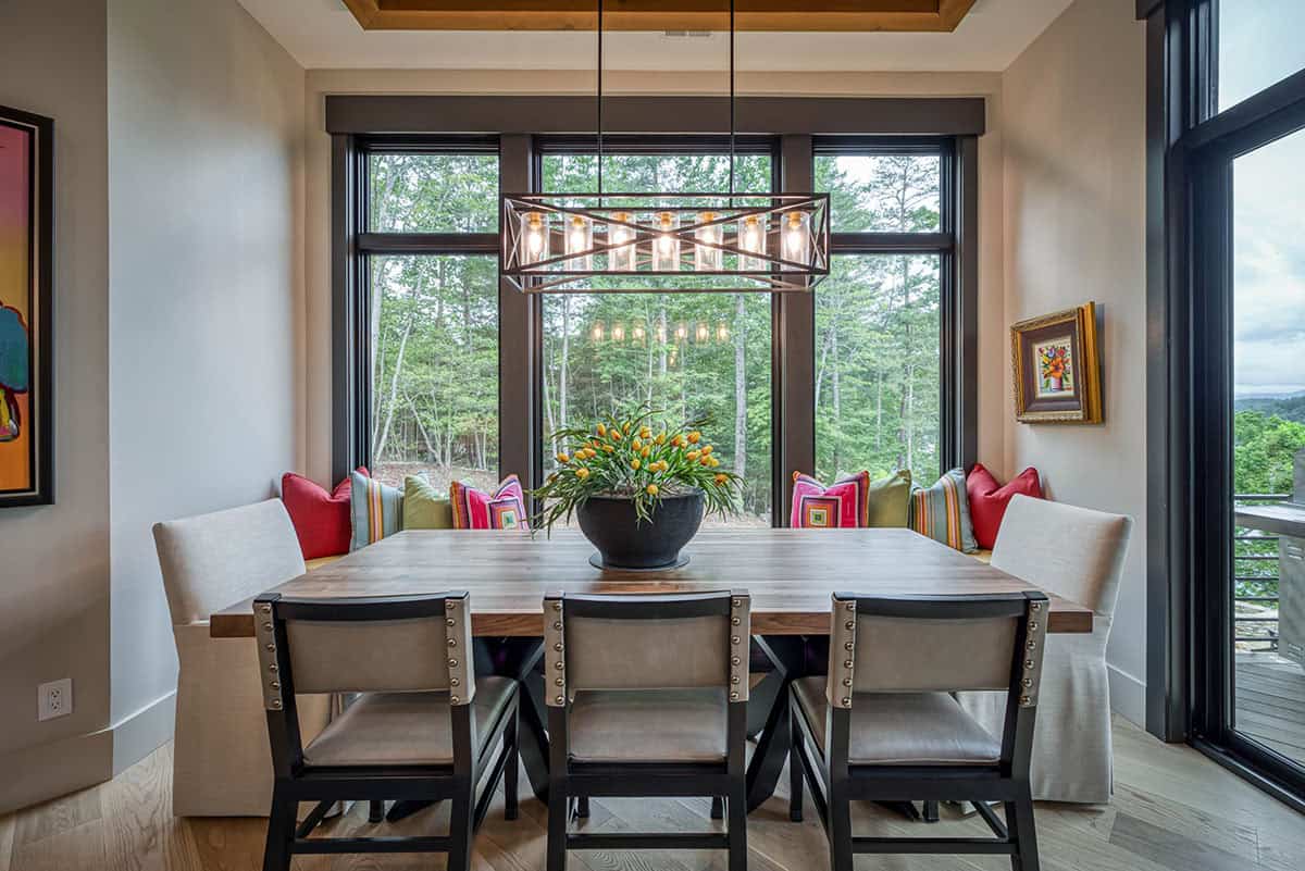 Dining nook with wood table, colorful throw pillows, and geometric chandelier by window