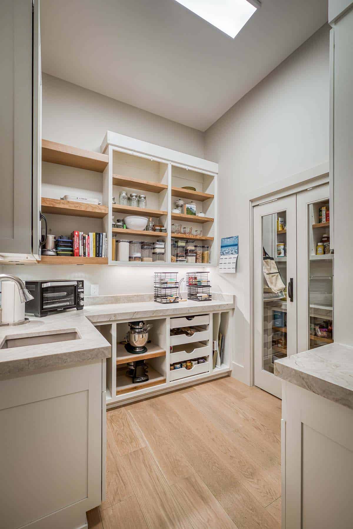 Wide view of butler's pantry with shelving, skylight, and glass pantry doors