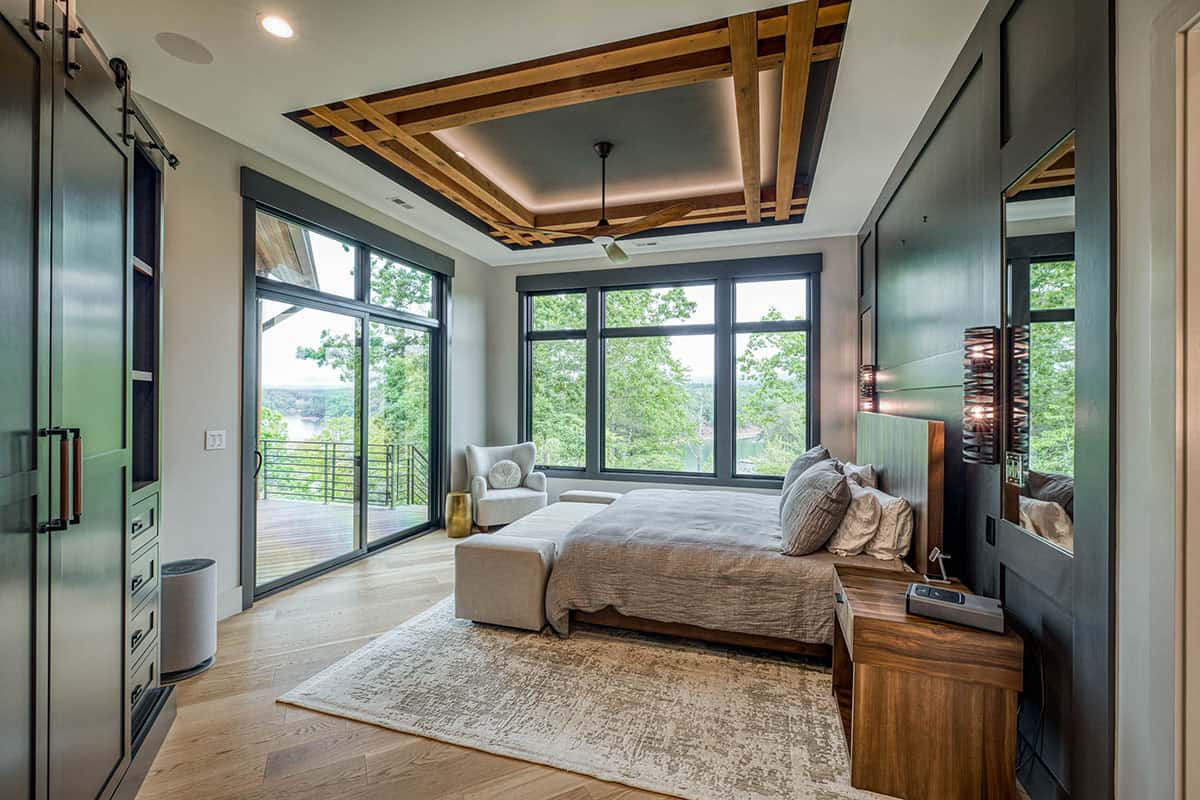 Bedroom with layered wood beam ceiling detail, ceiling fan, and lake-view sliding doors