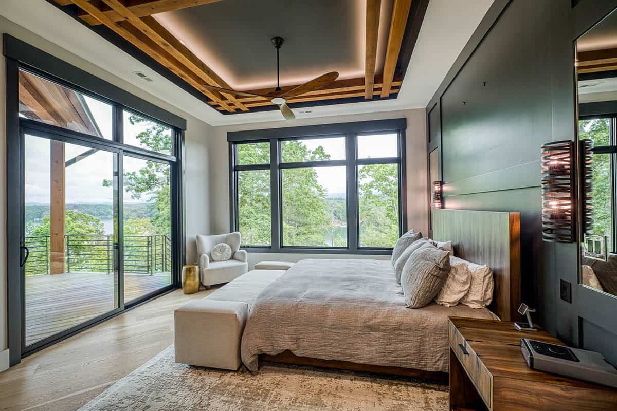 Bedroom with wood beam tray ceiling, dark accent wall, and sliding doors to deck