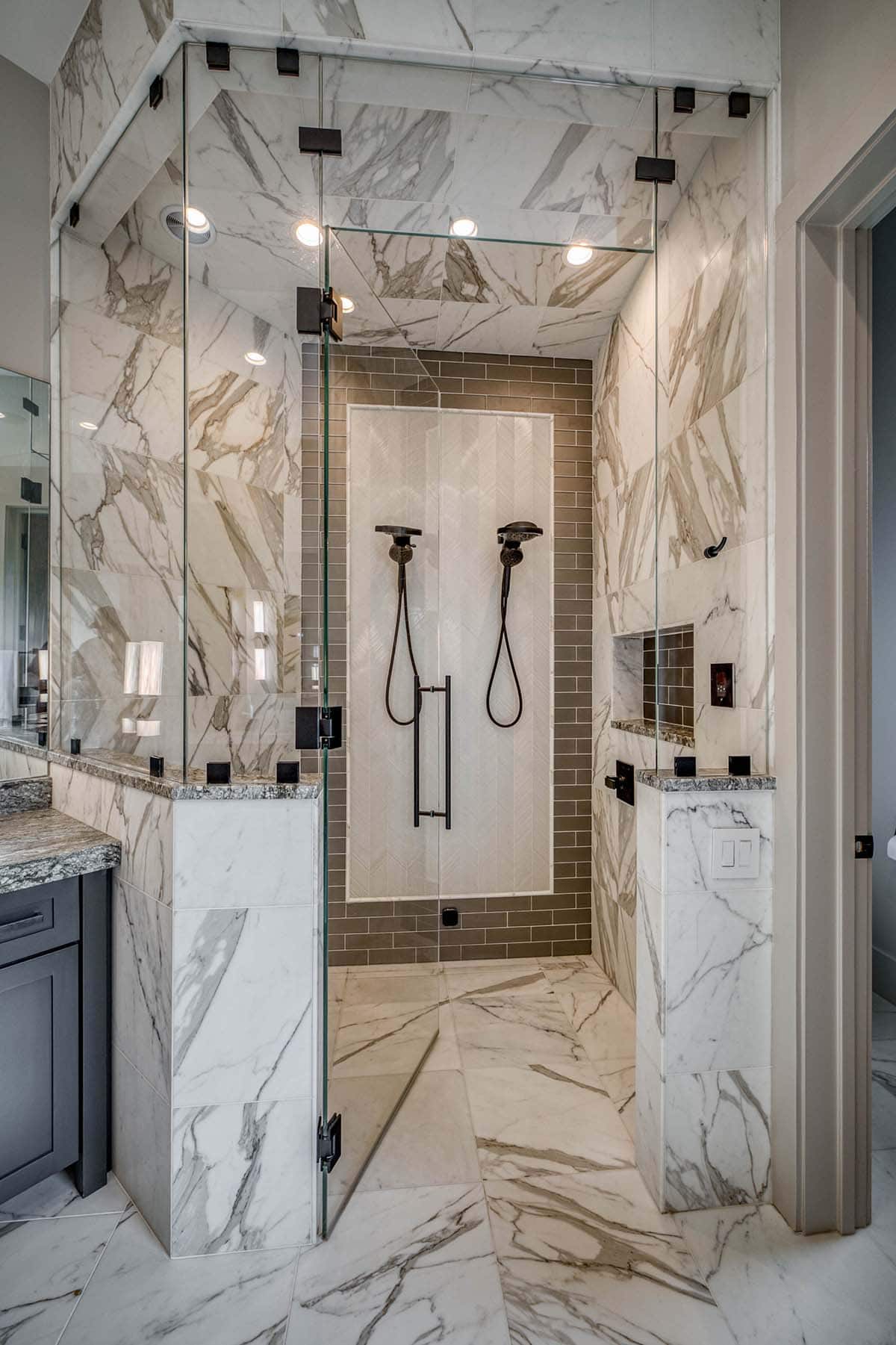 Marble-tiled walk-in shower with dual rainfall shower heads and glass enclosure