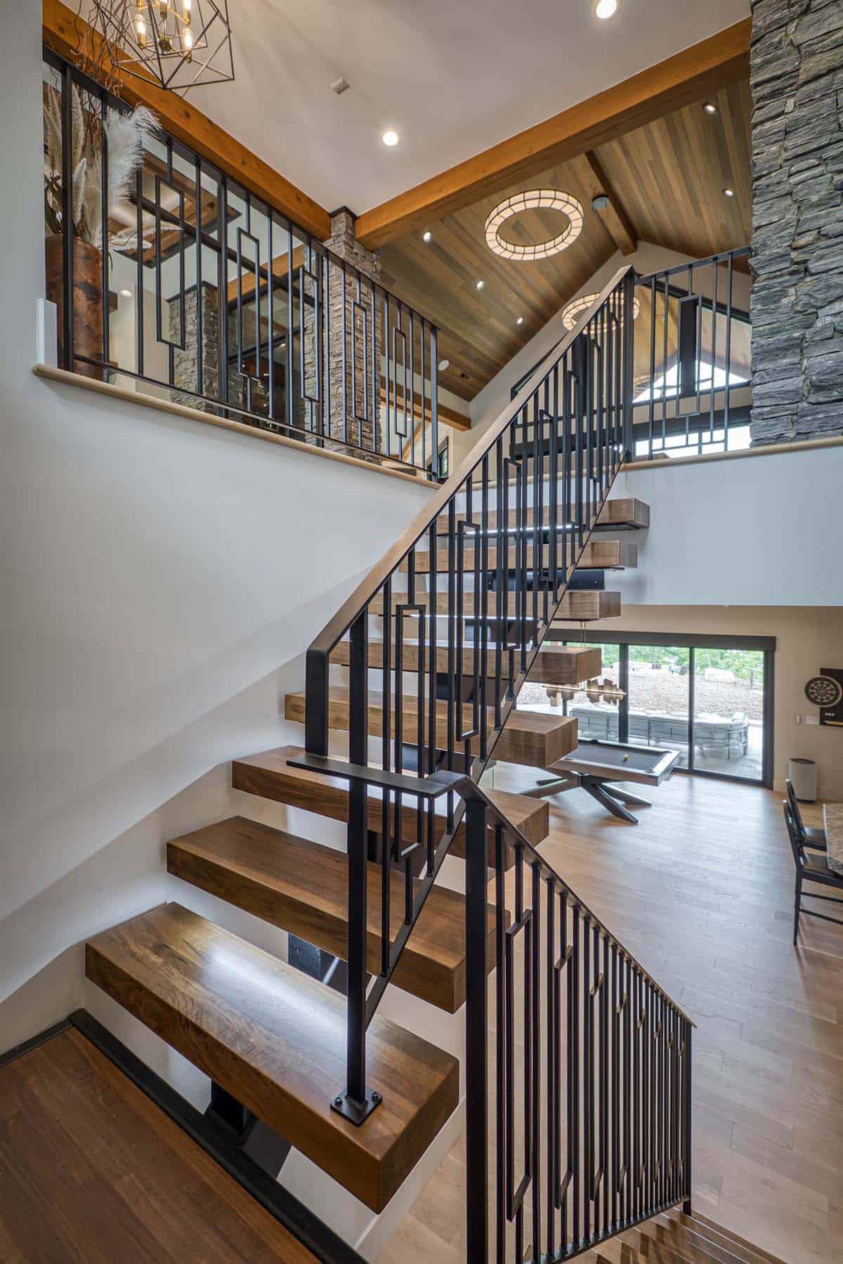 View down open staircase with floating wood treads, black railings, and game room below