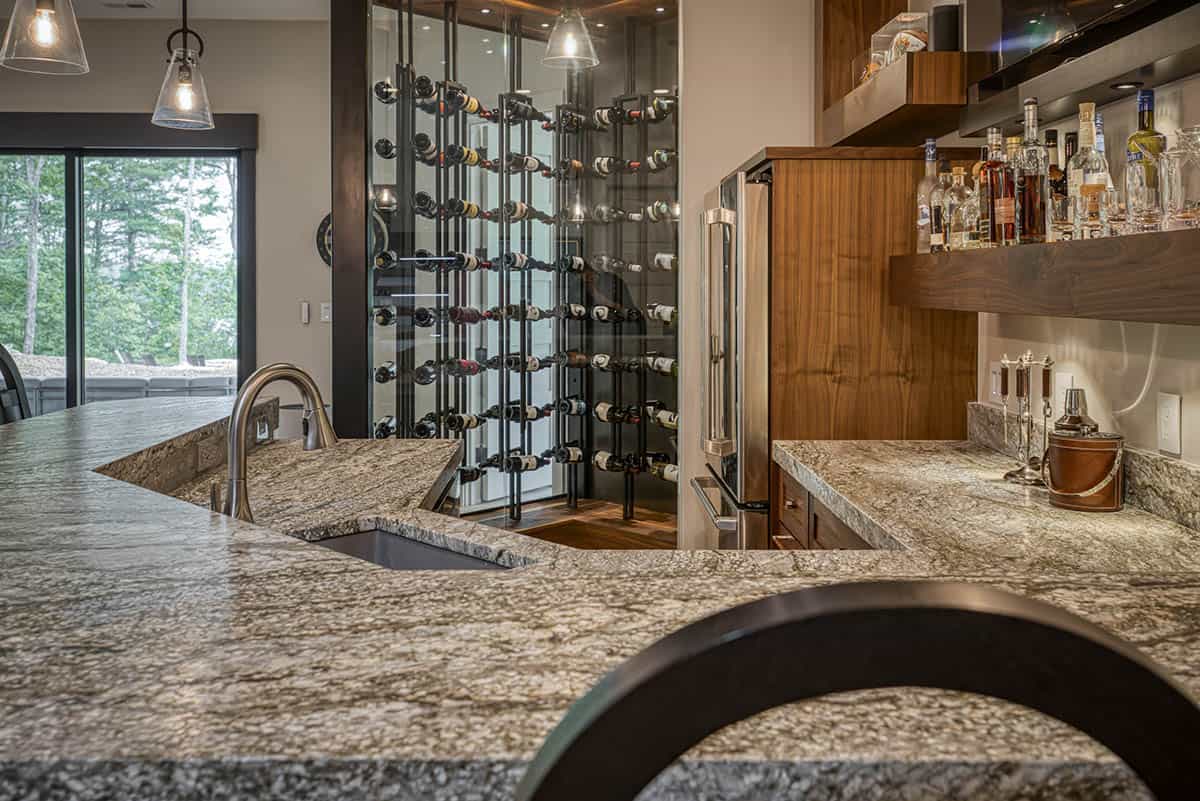 Close-up of granite bar counter with sink, wine wall, and wood cabinetry
