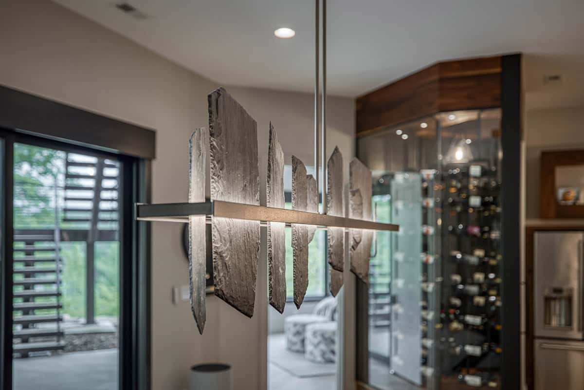 Close-up of sculptural stone-slat pendant light with wine cellar in background