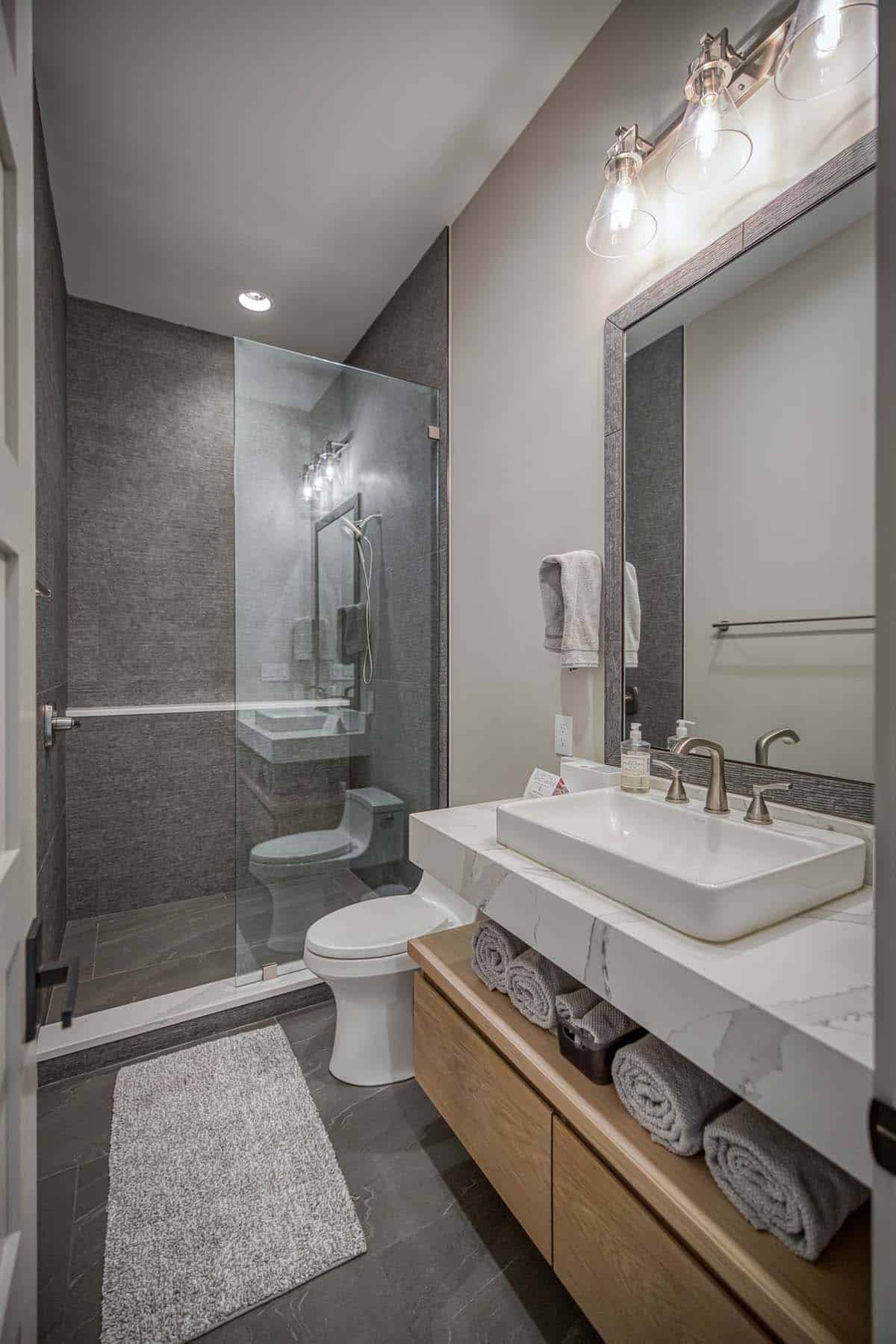Compact bathroom with glass shower, floating wood vanity, and marble countertop
