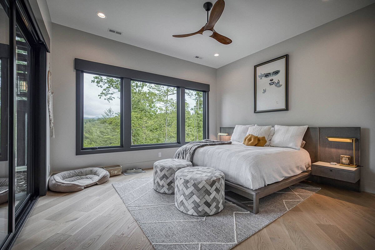 Bedroom with wood ceiling fan, dog bed, patterned rug, and forest-view windows
