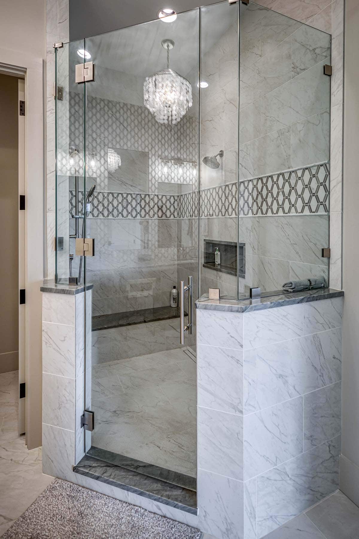 Glass-enclosed shower with patterned tile band, chandelier, and marble surround
