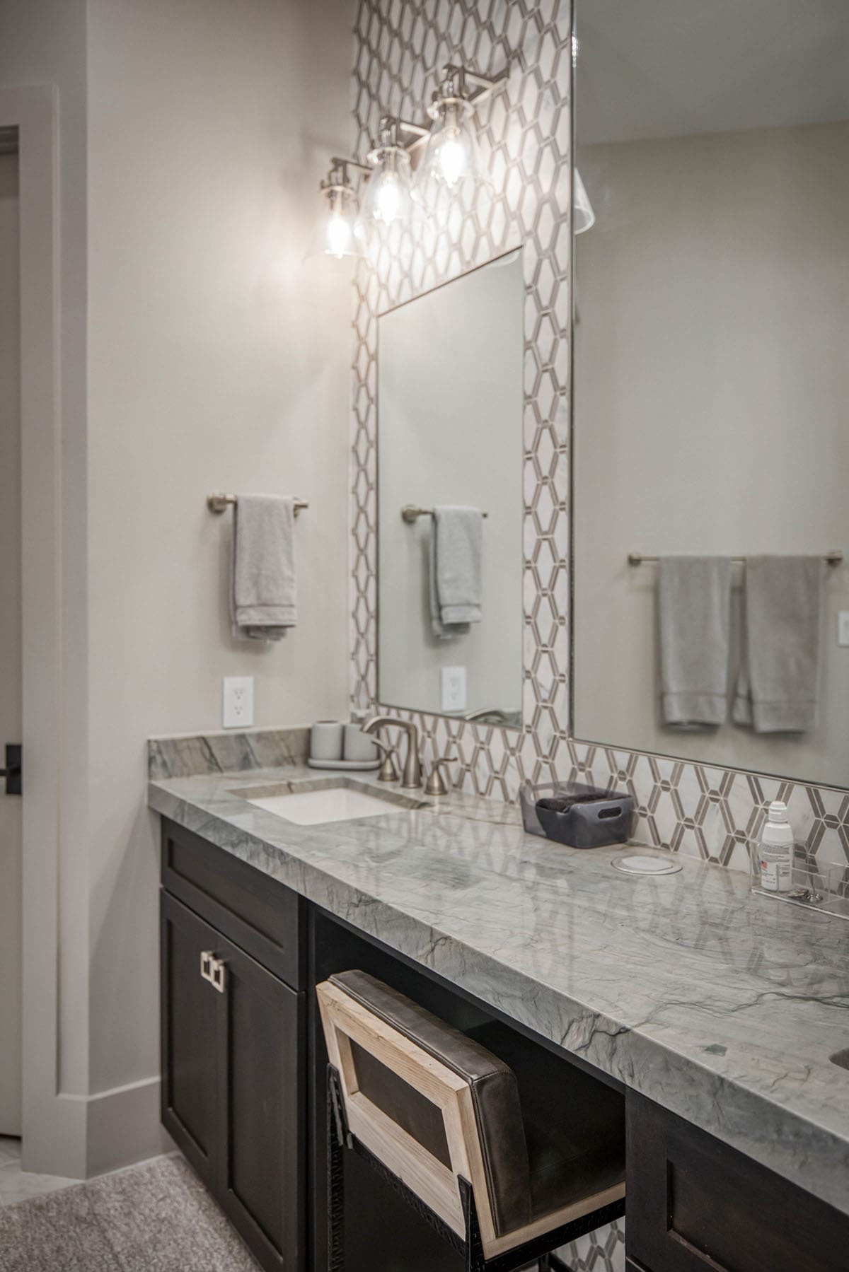 Close-up of bathroom vanity with marble counter, geometric tile backsplash, and towel bars