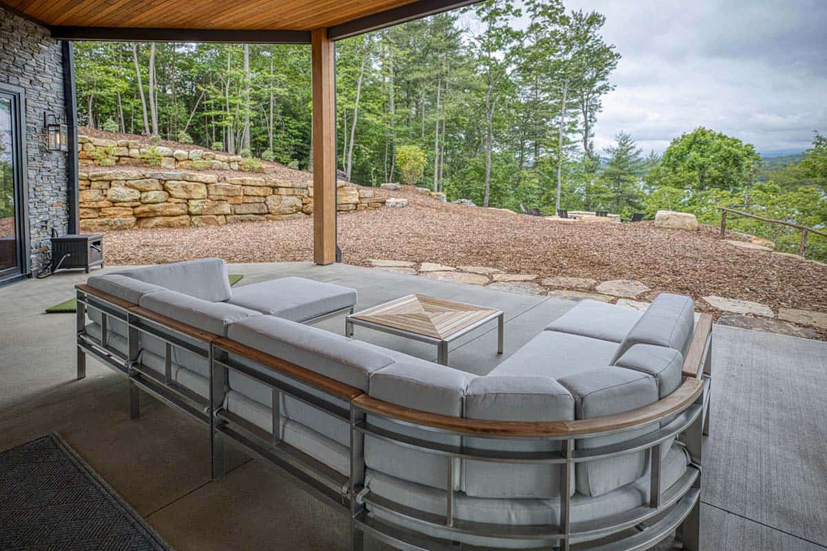 Curved outdoor sofa with wood-topped coffee table on covered patio overlooking stone terraced hillside