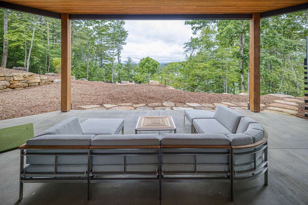 Covered patio framed by timber posts with curved sofa and distant lake view through trees