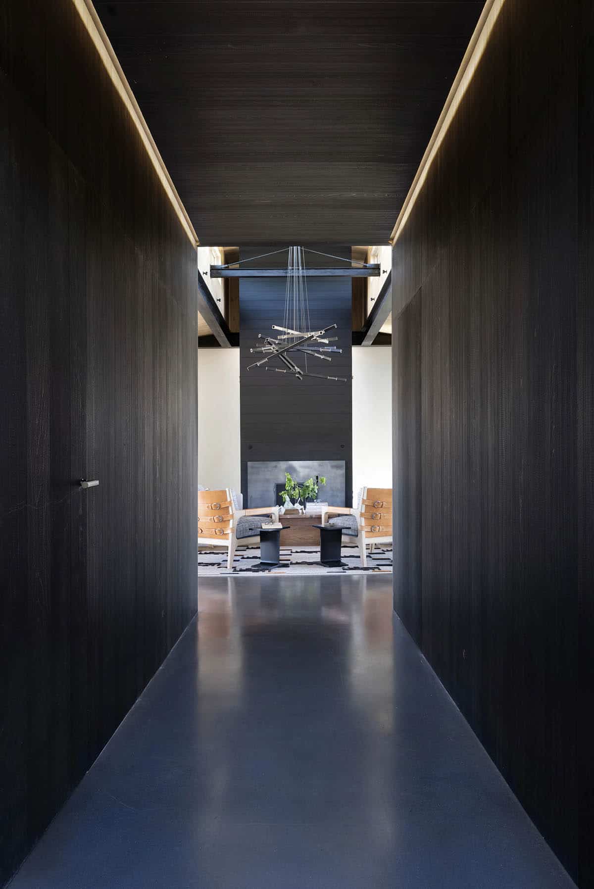 Dark wood-paneled hallway leading to a bright living room with a sculptural pendant light