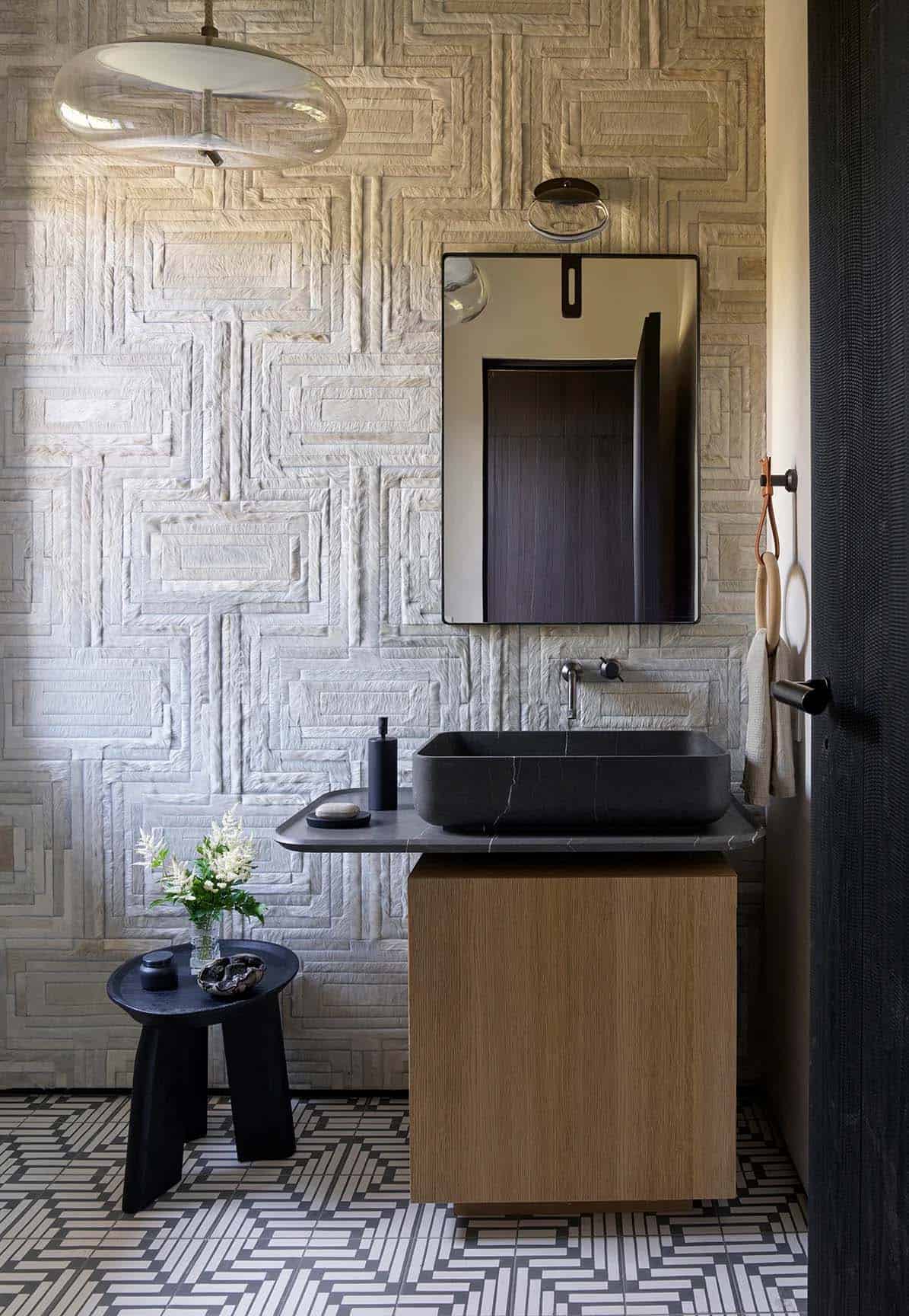 Powder room with textured woven wall covering, black stone vessel sink, and patterned tile floor