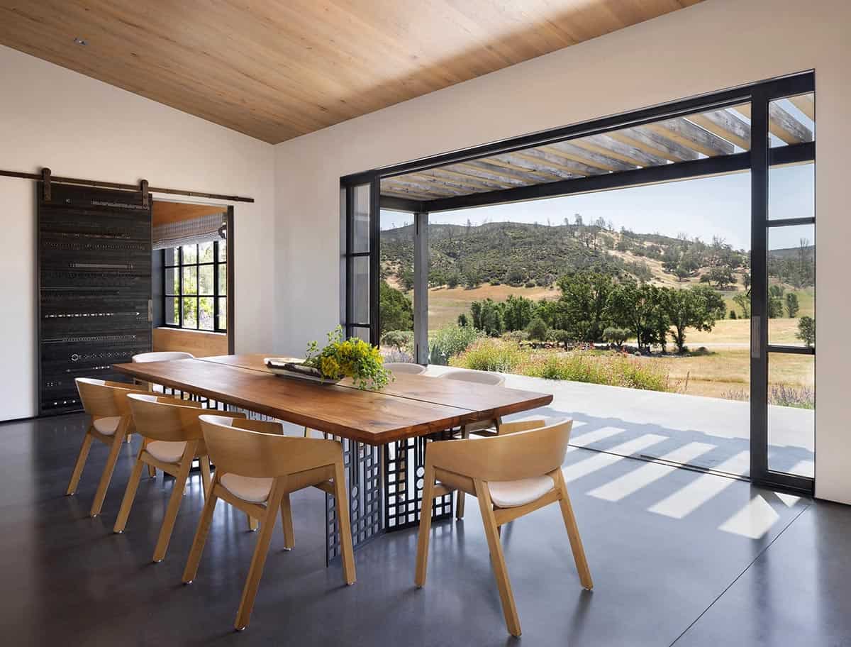 Dining area with live-edge wood table opening onto a covered patio and rolling hills view