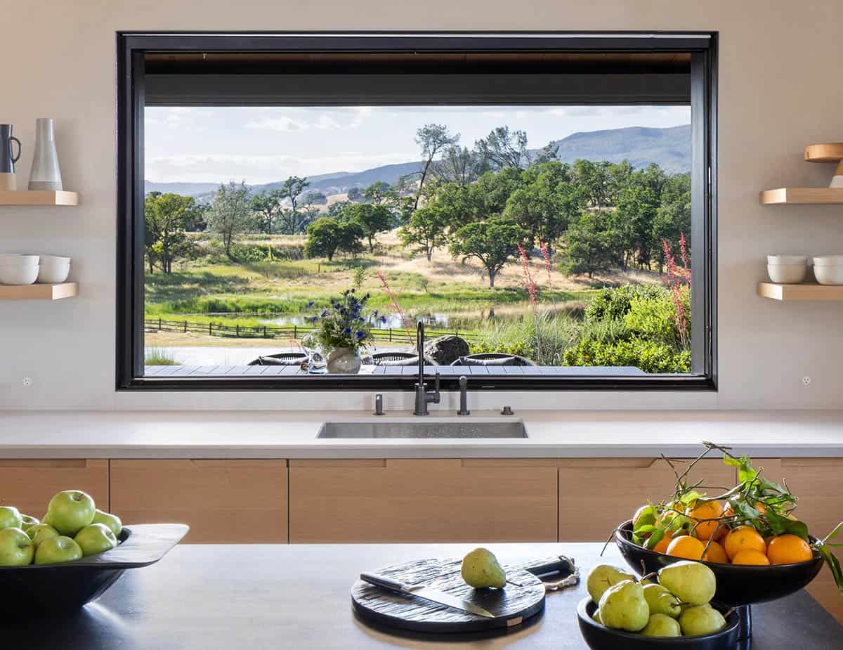 Kitchen window over the sink framing a pastoral view of trees, hills, and a pond