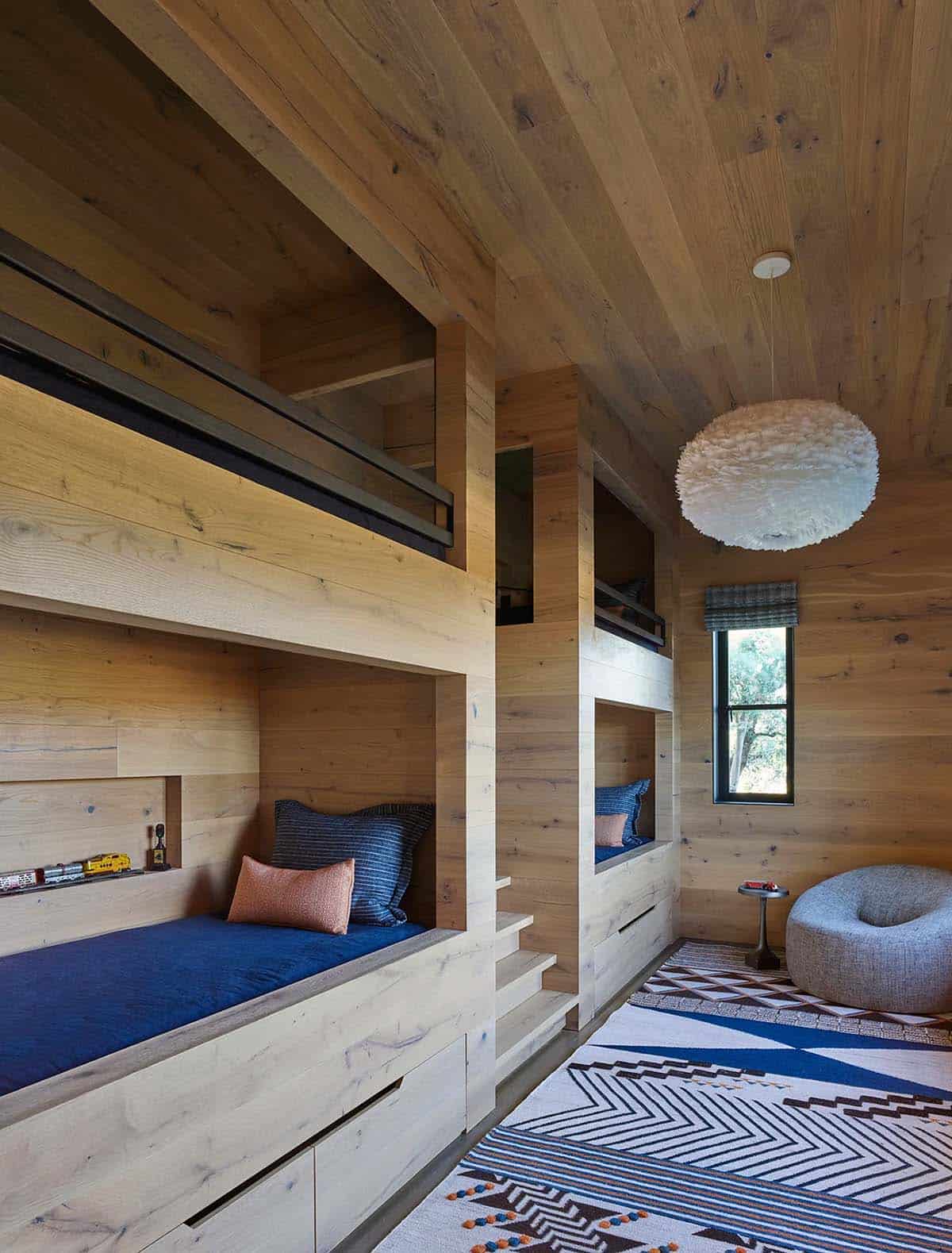 Built-in wood bunk beds with blue bedding and a fluffy white pendant light