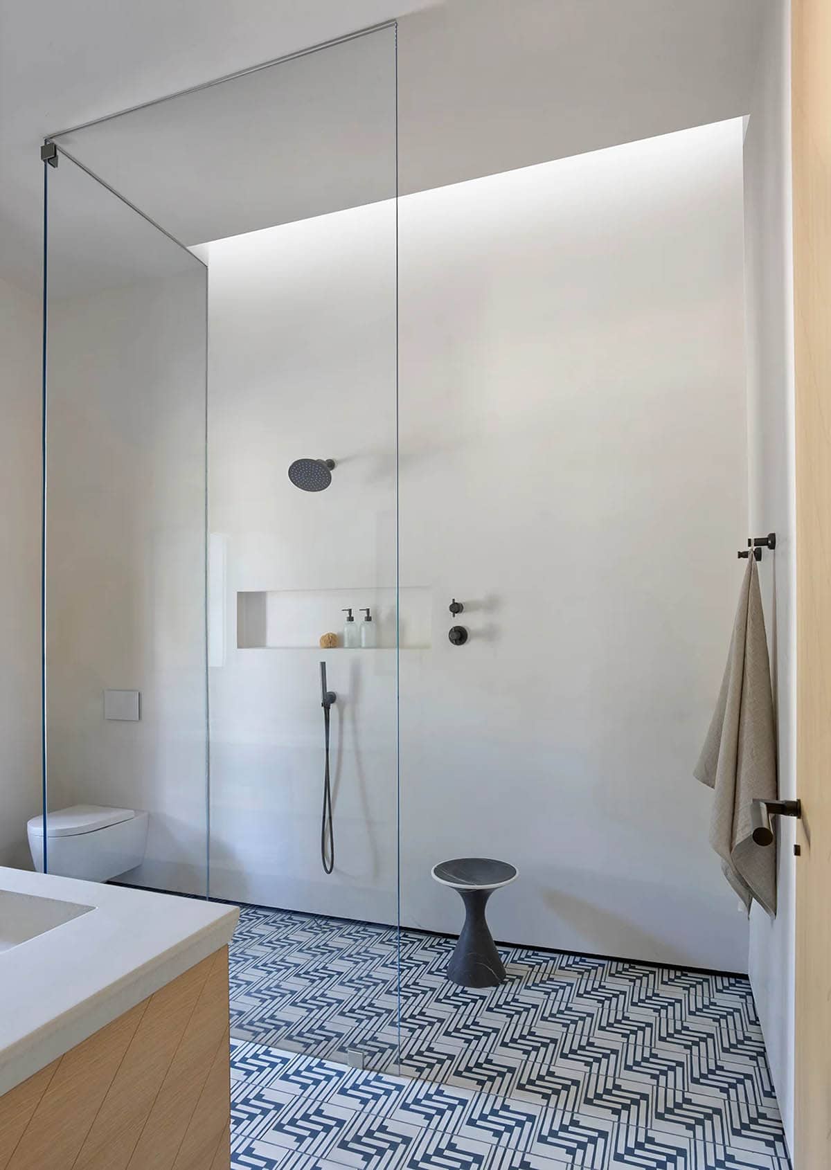 Minimalist glass-walled shower with skylight and patterned tile flooring