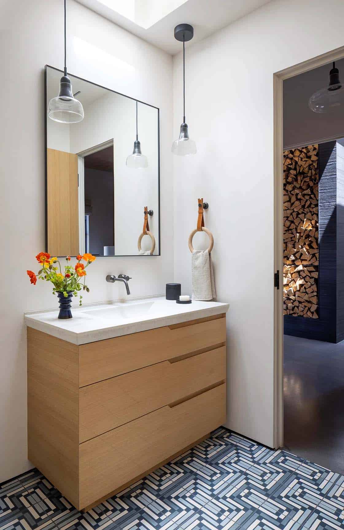 Small powder room with wood vanity, mirror, and glimpse of a stacked firewood display