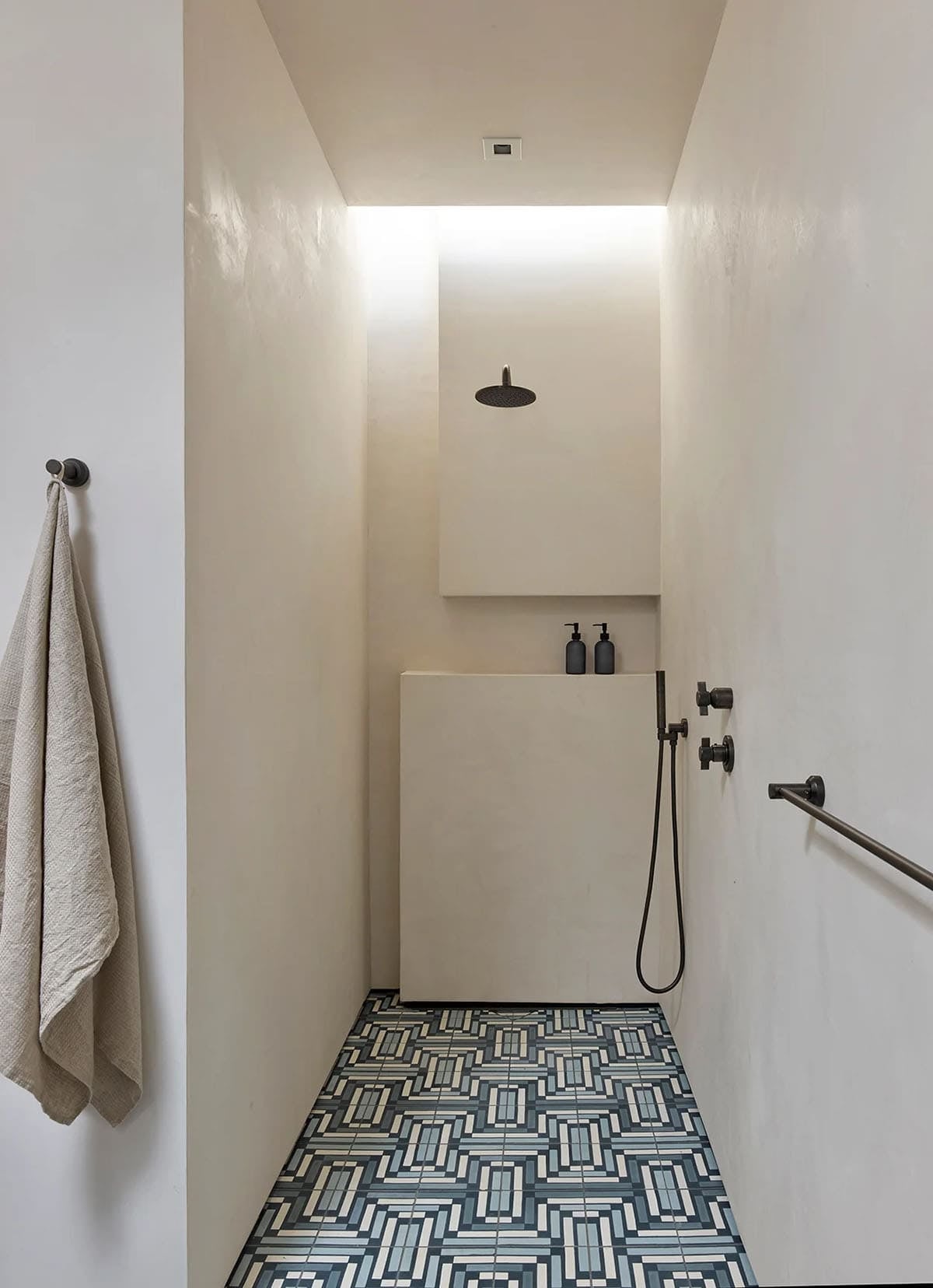Plaster-walled walk-in shower with geometric tile floor and black fixtures
