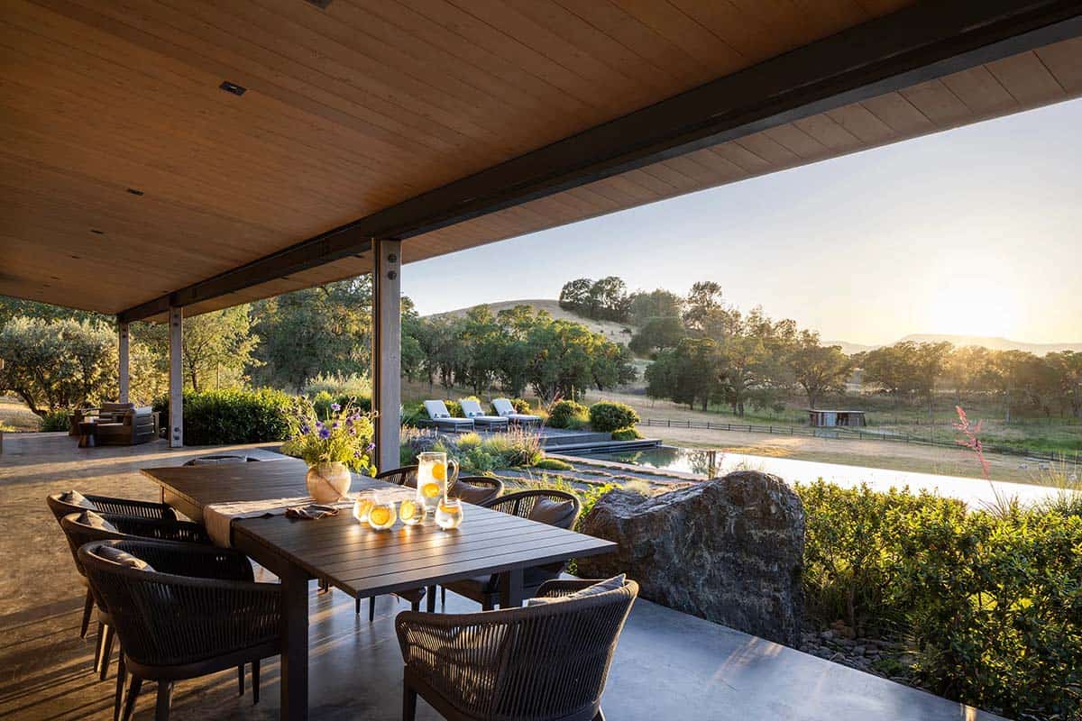 Covered outdoor dining patio overlooking a pond and hillside at sunset