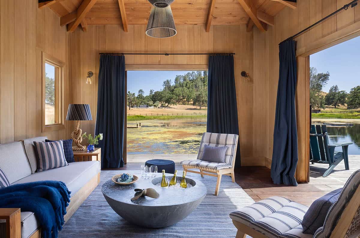 Wood-paneled boathouse lounge with striped upholstery and curtains open to the pond