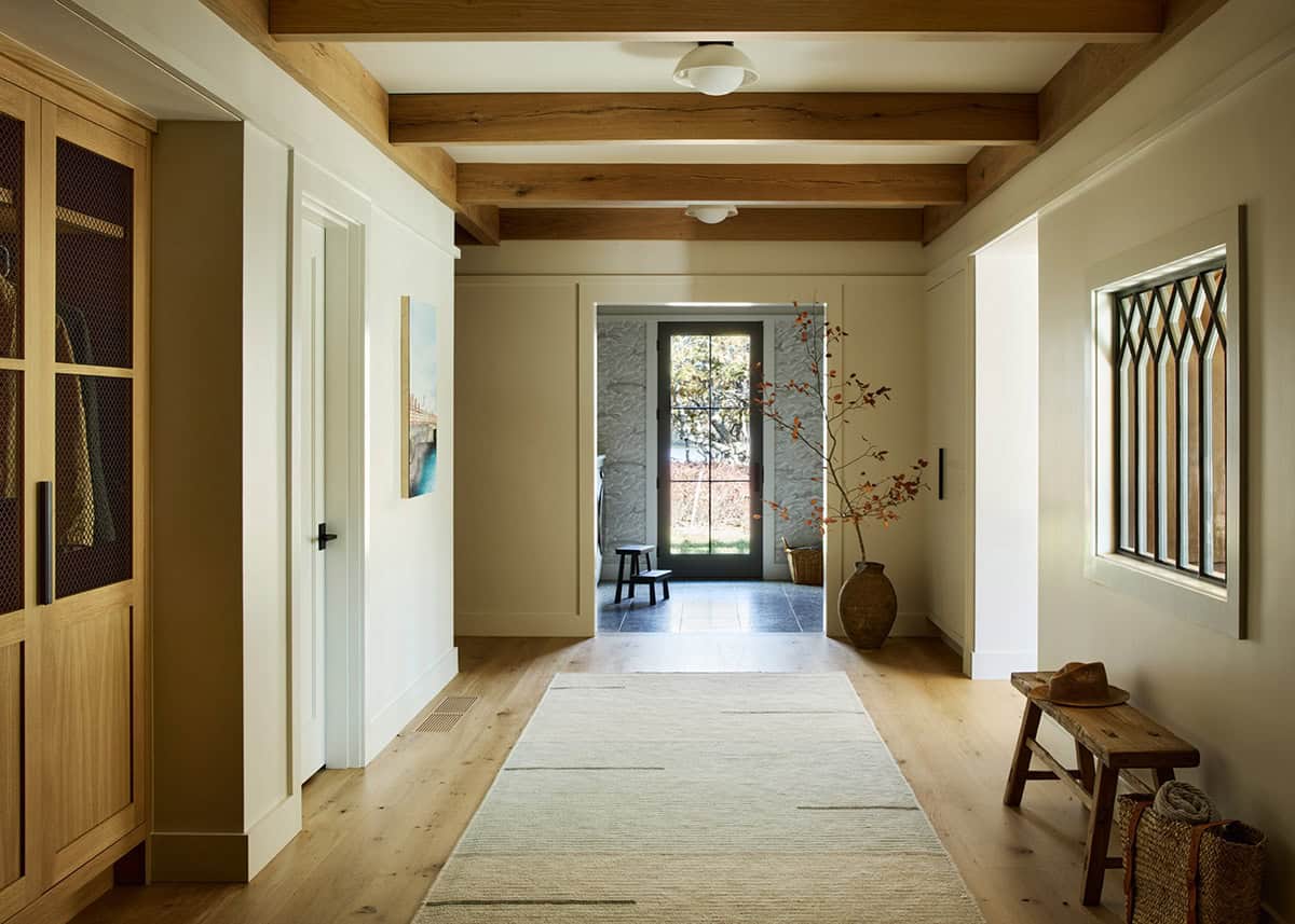 Beam-ceilinged hallway with a leaded glass window and stone entry beyond